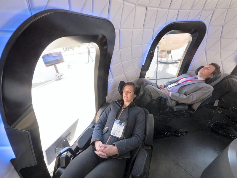 Attendees sit inside the high fidelity crew capsule mock up of the Blue Origin LLC New Shepard system during the Space Symposium in Colorado Springs, Colorado, U.S., on Wednesday, April 5, 2017. Jeff Bezos, chief executive officer of Amazon.com Inc. and founder of Blue Origin, has been reinvesting money he made at Amazon since he started his space exploration company more than a decade ago, and has plans to launch paying tourists into space within two years. Photographer: Matthew Staver/Bloomberg