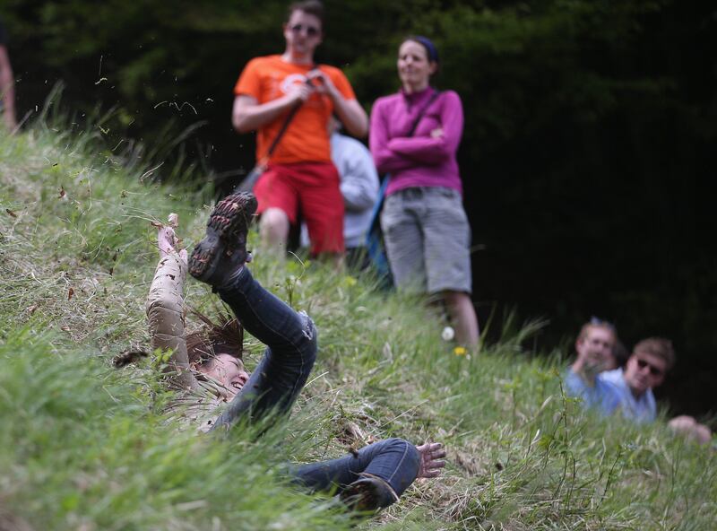 BROCKWORTH, ENGLAND - MAY 27:  A woman falls down the steep gradient of Cooper's Hill during the annual Bank Holiday tradition of cheese-rolling on May 27, 2013 in Brockworth, Gloucestershire, England. Although no longer a officially organised event since 2009, thousands of spectators still gathered to watch contestants from around the world tumbling down the 200m slope, which has a 1:1 gradient in parts, in a series of races that are said to date back hundreds of years, with the winner of each receiving a cheese. Injuries such as broken arms and legs are commonplace.  (Photo by Matt Cardy/Getty Images) *** Local Caption ***  169553493.jpg