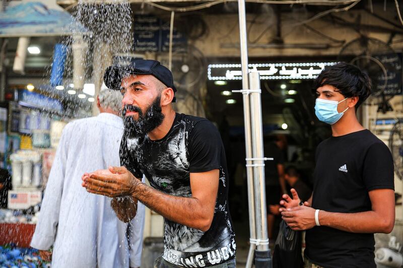 A man stands underneath a roadside shower along Sinak street in Iraq's capital Baghdad on August 9, 2020, to cool off due to extremely high temperature rises amidst a heatwave.  / AFP / AHMAD AL-RUBAYE
