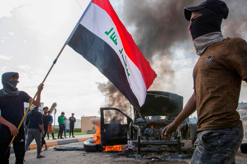 Iraqi demonstrators stand next to the smoking remains of an Iraqi anti-riot vehicle during a demonstration in the southern city of Basra. AFP