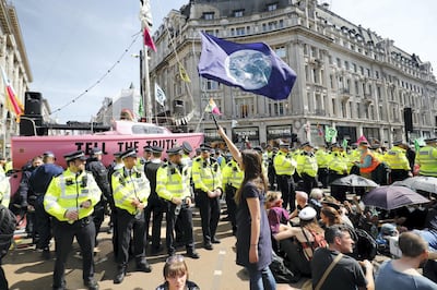 A climate change activist waves a flag as police officers keep watch during the ocupation of the road junction at Oxford Circus in central London on April 19, 2019, the fifth day of an environmental protest by the Extinction Rebellion group. - Undeterred by over 400 arrests, climate change activists continued their demonstration into a fifth day in London with a small protest at the country's main Heathrow Airport, along with the ongoing protest camps at other iconic locations around the British capital. (Photo by Tolga AKMEN / AFP)