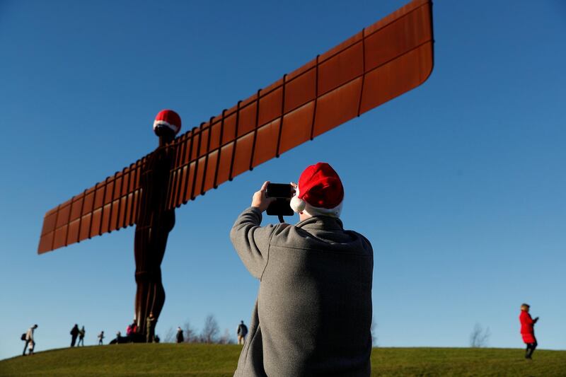Passerby takes pictures of the Angel of the North statue adorned with Santa Claus' hat in Gateshead, Britain. Reuters