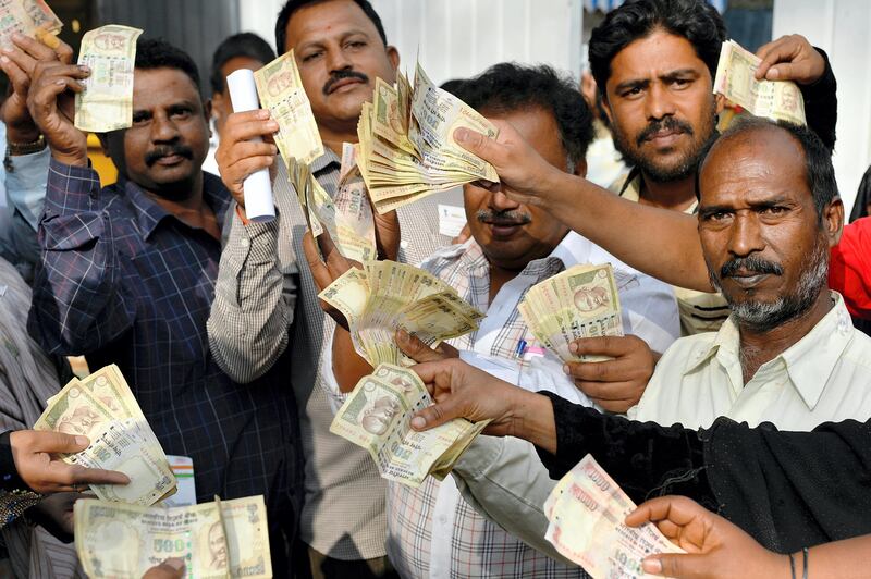 People waiting to exchange demonitised Indian currency, show their old 500 and 1000 Rupee notes near the closed gates of Reserve Bank of India in Bangalore on January 2, 2017 after acceptence of the banned notes at banks and RBI ended two days ago. / AFP PHOTO / Manjunath KIRAN