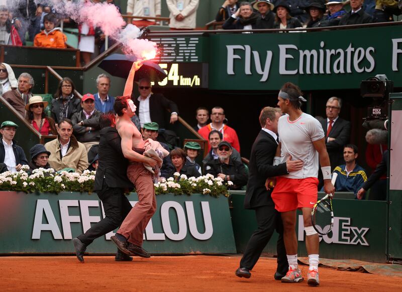 *** BESTPIX *** PARIS, FRANCE - JUNE 09: Rafael Nadal of Spain looks on as security guards restrain a protester after he lit a flare and ran on court before the start of a game in the Men's Singles final match between Rafael Nadal of Spain and David Ferrer of Spain during day fifteen of the French Open at Roland Garros on June 9, 2013 in Paris, France.  (Photo by Matthew Stockman/Getty Images) *** Local Caption ***  170229538.jpg