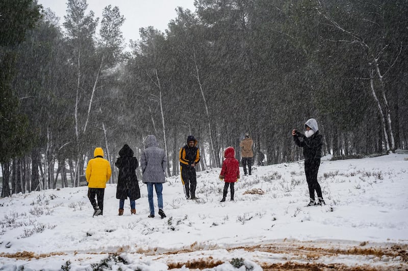 People walk in the snow outside a forest in the Sidi al-Hamri region of Libya's eastern Jebel Akhdar (Green Mountain) upland region, about 200 kilometres east of Benghazi, on February 16, 2021. (Photo by - / AFP)