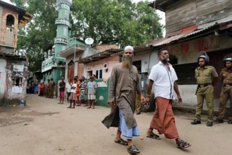 Sri Lankan Muslims walk past a vandalised mosque as police stand guard in Colombo.