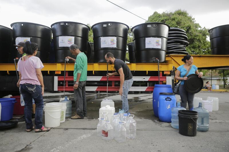 People fill containers with water from tanks in a service area in Caracas, Venezuela. Getty Images