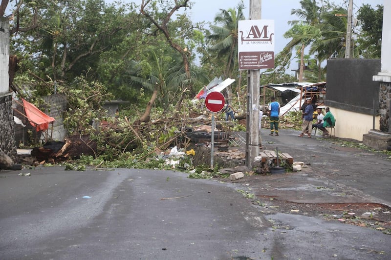 People stand by fallen trees on April 25, 2019 in Moroni after tropical storm Kenneth hit Comoros before heading to recently cyclone-ravaged Mozambique. Cyclone Kenneth passed the Indian Ocean archipelago nation Comoros today but its effects, including high winds and heavy rains, were still being felt, the country's Meteorological Office wrote on Facebook. / AFP / Ibrahim YOUSSOUF

