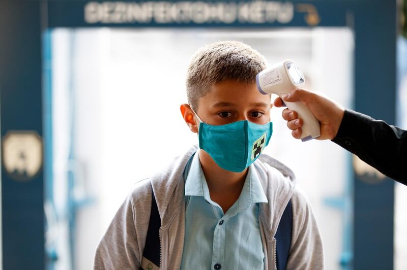 A staff member checks the body temperature of an elementary school pupil, on the first day of school in Pristina, Kosovo. EPA