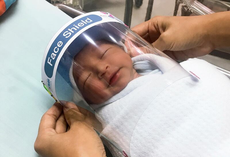 A nurse adjusts tiny face shield for a newborn baby to protect from new coronavirus at the newborn nursery of the hospital in Samutprakarn province, central Thailand.  AP