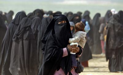 TOPSHOT - A fully veiled woman holds her baby as civilians fleeing the Islamic State's group embattled holdout of Baghouz walk in a field on February 13, 2019 during an operation by the US-backed Syrian Democratic Forces (SDF) to expel the Islamic State group from the area, in the eastern Syrian province of Deir Ezzor. Syrian fighters backed by artillery fire from a US-led coalition battled a fierce jihadist counteroffensive as they pushed to retake a last morsel of territory from the Islamic State group in an assault lasting days. More than four years after the extremists declared a "caliphate" across large parts of Syria and neighbouring Iraq, several offensives have whittled that down to a tiny scrap of land in eastern Syria. / AFP / Delil souleiman

