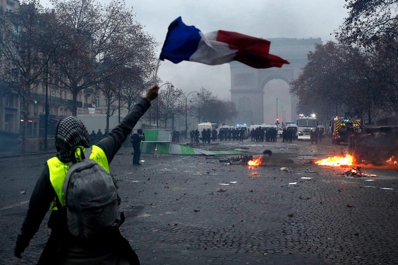 A protester wearing a yellow vest waves a French flag during clashes with riot police near the Arc de Triomphe in Paris. EPA