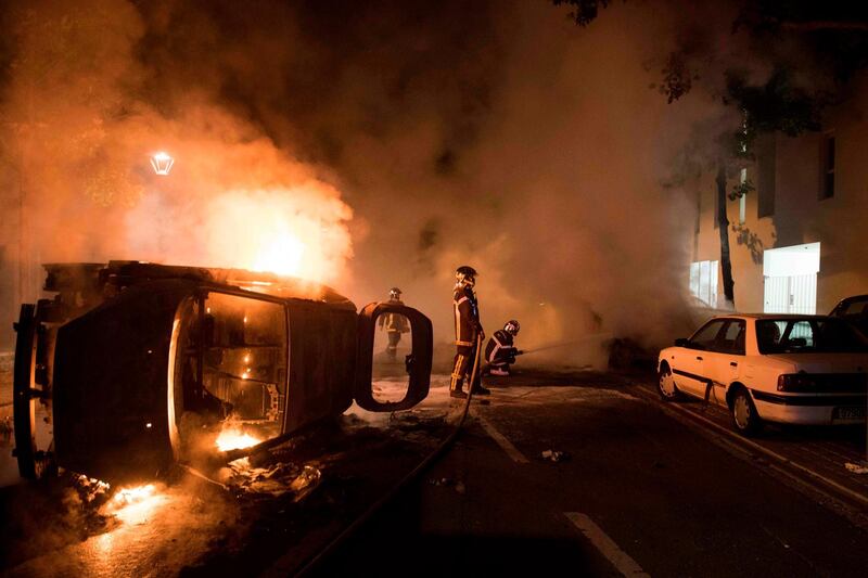 TOPSHOT - Firefighters work to put out a fire near a burning car in the Malakoff neighborhood of Nantes early on July 4, 2018.  Groups of young people clashed with police in the western French city of Nantes on the night of July 3 after a man was shot dead by an officer during a police check. Cars were burned and a shopping centre partly set alight in the Breil neighbourhood as police confronted young people, some armed with molotov cocktails. / AFP / SEBASTIEN SALOM GOMIS
