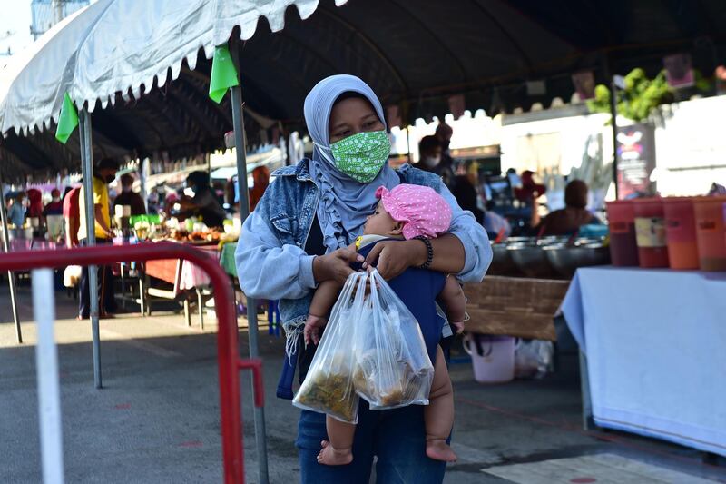 A woman holding a child walks with food in a market in Thailand's southern province of Narathiwat.   AFP