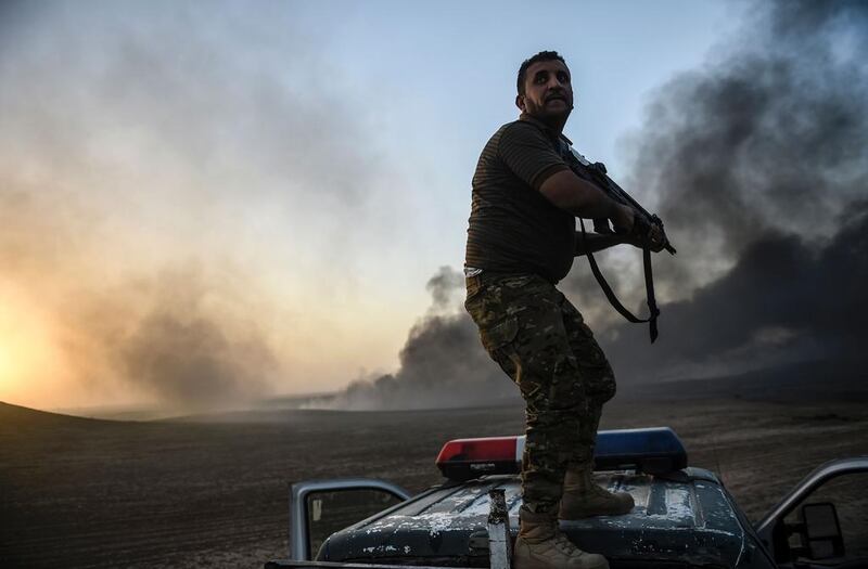 A member of the Iraqi government forces takes a position  on top of a vehicle as smoke rises on the outskirts of the Qayyarah area, some 60 kilometres south of Mosul, during an operation against ISIL to retake the main hub city. Bulent Kilic / AFP