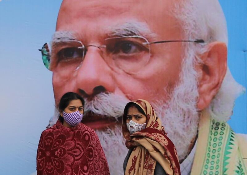 People wearing protective masks stand in front of a poster featuring a photograph of India's Prime Minister Narendra Modi outside the All India Institute of Medical Sciences in New Delhi, India. India launched one of the world’s largest coronavirus vaccination drives on Saturday, setting in motion a complex deployment plan aimed at stemming the wide spread of infections across a nation of more than 1.3 billion people. Bloomberg