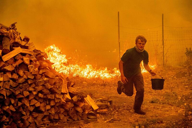 Alex Schenck carries a water bucket while fighting to save his home as the Ranch Fire tears down New Long Valley Rd near Clearlake Oaks, California. Noah Berger/AFP