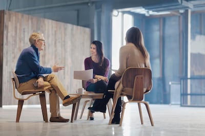 Business colleagues people gathered in lounge area meeting space open air lobby free flowing ambient lighting daylight copyspace talking about planning strategy ideas together senior adult man women paperwork documents coffee table legs crossed casually dressed casual mobile phone smart phone positive emotion connection laughing smiling interactivity breaking new ground generations age gap inspiration innovation co-working startup tech company freelancers entrepreneur contemporary modern small business. Getty Images