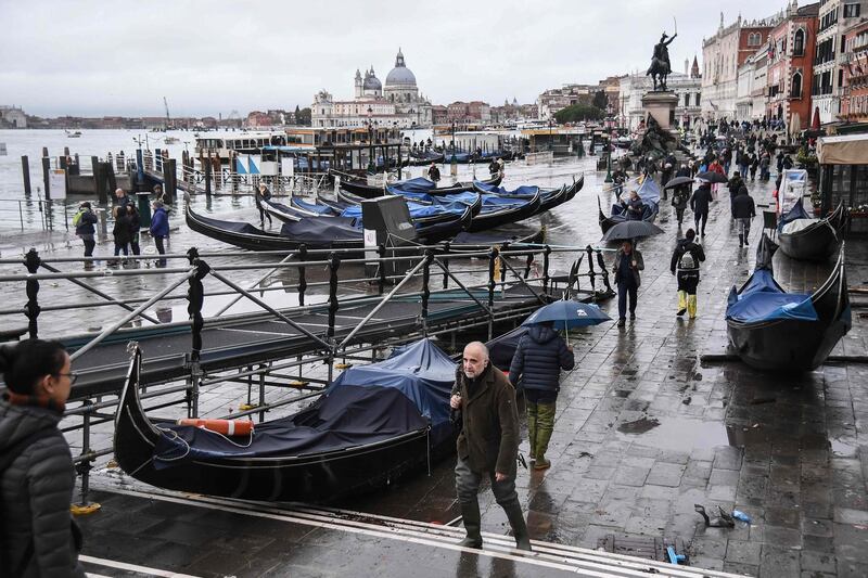 People walk past stranded gondolas washed away at Riva degli Schiavoni. AFP