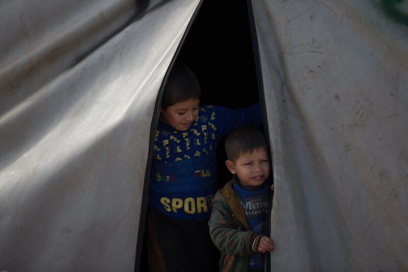 A child stands next to his brother at the entrance to their tent as they look at the snow in the camp.