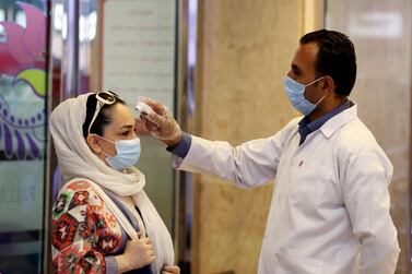 A woman wearing a protective face mask to help prevent spread of the coronavirus has her temperature checked as she enters a shopping centre in Tehran, Iran. AP Photo