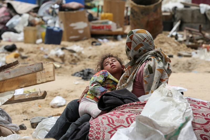 A Palestinian mother holds her sleeping child after fleeing Rafah due to an Israeli military operation. Reuters