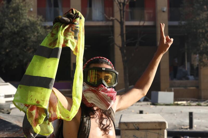 A Lebanese anti-government protester flashes a victory sign and holds a blood-stained yellow jacket of a fellow protester during clashes with riot police.  EPA
