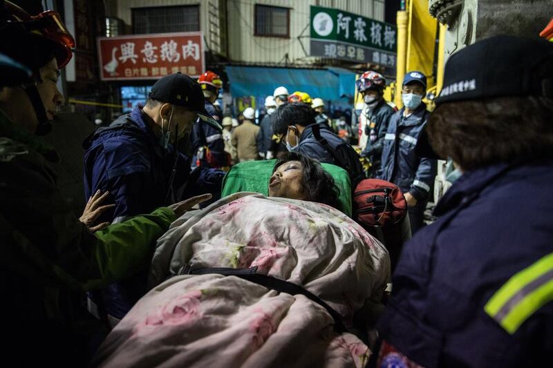 A woman is taken to an ambulance by rescue workers after being extracted by a crane from the rubble of a collapsed building in the southern Taiwanese city of Tainan. On Sunday, thousands of rescuers in red, orange, yellow and black uniforms worked on different levels of the folded building, which was supported by steel pillars. Anthony Wallace / AFP
