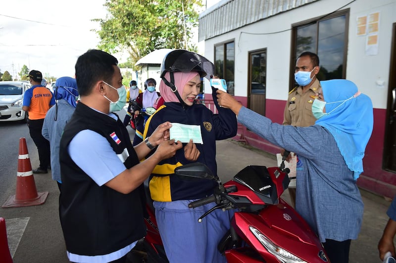 A woman on a scooter has her temperature taken and is given a facemask at a checkpoint set up to examine people in a bid to halt the spread of the Covid-19 coronavirus in the southern Thai province of Narathiwat.  AFP