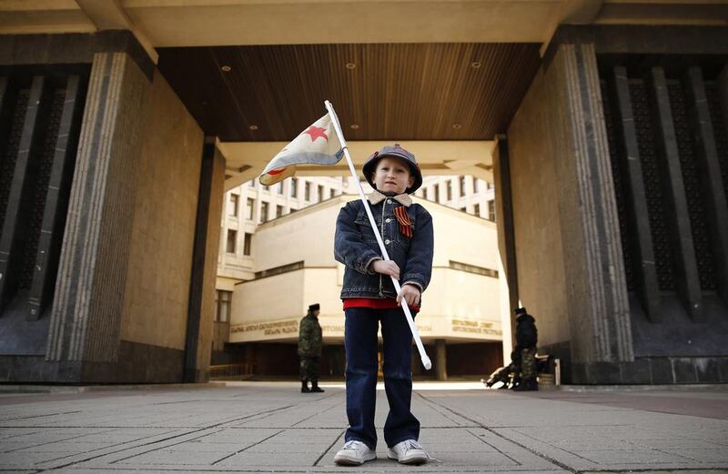 A boy stands in front of the Crimean parliament building, with members of Crimean self-defence units seen in the background, Thomas Peter / REUTERS