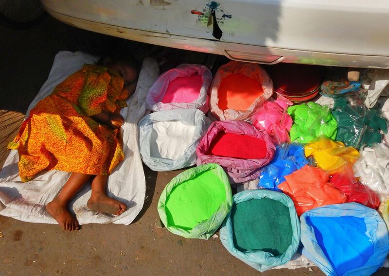 A young girl sleeps next to bags of coloured powder next to a car at a market in New Delhi, India.  AFP