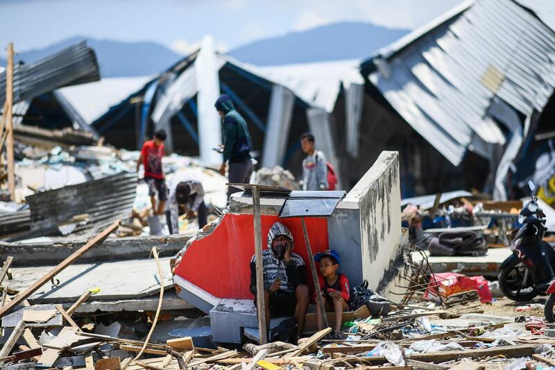 Survivors take a break as they salvage items from the debris of a factory complex in Palu. AFP
