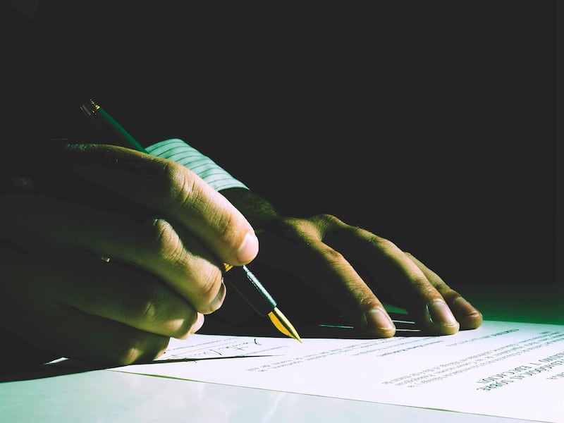 Close up Human Hand Signing on Formal Paper at the Table on Black Background. Retro Filter Effect. Getty Images