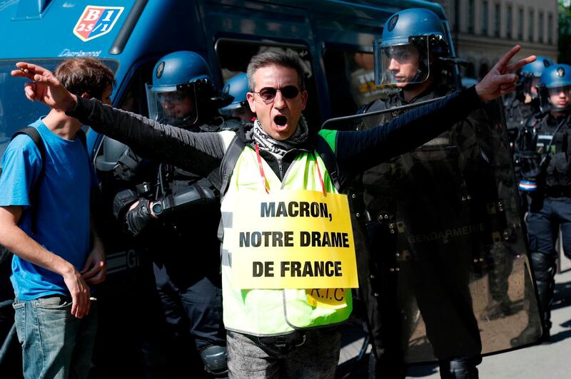 A protester wearing a 'Yellow Vest' (gilet jaune) and sporting a sign reading (a play on word) "Macron, our French drama" in reference to the fire that devastated the Notre-Dame de Paris Cathedral, takes part in an anti-government demonstration in Paris on April 20, 2019. 'Yellow vest' movement protesters take to the streets on April 20, 2019 for 23rd consecutive Saturday. / AFP / Zakaria ABDELKAFI
