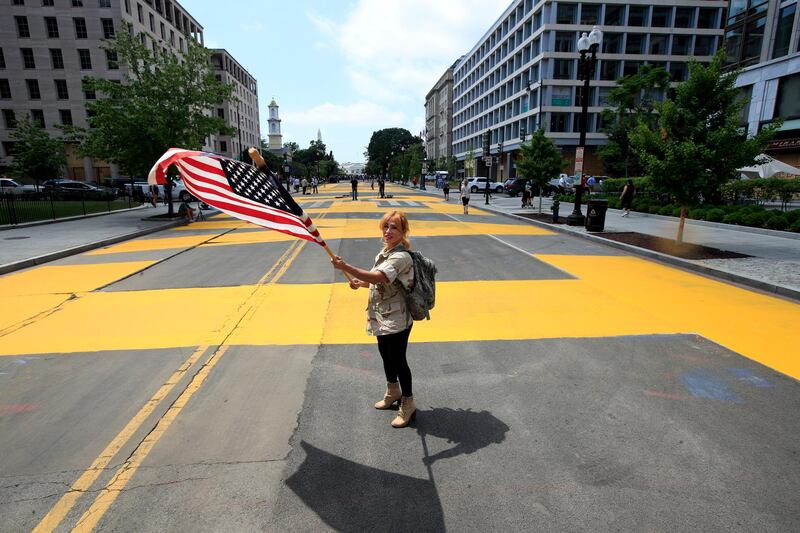 Beth Shafa waves an American Flag near the White House, Friday, June 5, 2020, in Washington. City workers and activists painted the words Black Lives Matter in enormous bright yellow letters on the street leading to the White House, a highly visible sign of the District of Columbia's embrace of a protest movement that has put it at odds with President Donald Trump. (AP Photo/Manuel Balce Ceneta)