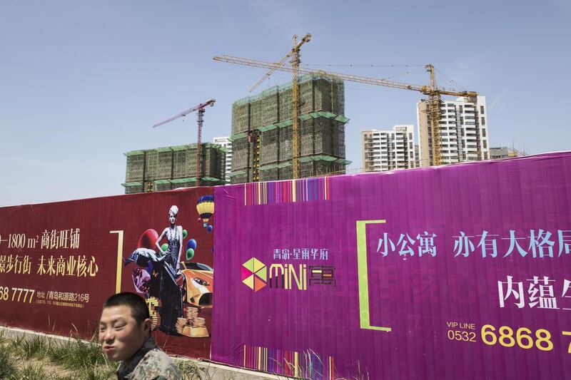 A man stands in front of residential buildings under construction in Qingdao, China, on Tuesday, May 8, 2018. China is scheduled to release new home price figures on May 16. Photographer: Qilai Shen/Bloomberg