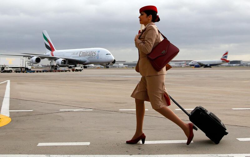 An Emirates air stewardess pulls a luggage case as she walks in the tarmac near one of the airline's Airbus A380 aircraft, at Terminal 3 of Heathrow Airport in London, U.K., on Thursday, Dec. 5, 2013. Emirates, the world's largest buyer of Airbus A380 aircraft, is exploring engine options for a batch of 50 additional superjumbos, handing Rolls-Royce Holdings Plc an opportunity to unseat a General Electric Co. and Pratt & Whitney joint venture that powers the existing jets. Photographer: Paul Thomas/Bloomberg