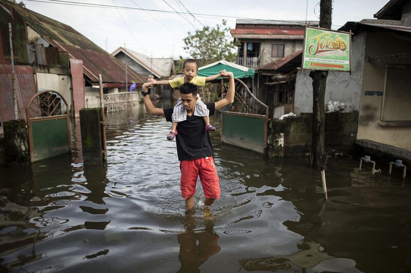 A father carries his son on his shoulders as they cross a flooded street in the aftermath of Super Typhoon Mangkhut in San Simon, Pampanga on September 16, 2018. / AFP / NOEL CELIS
