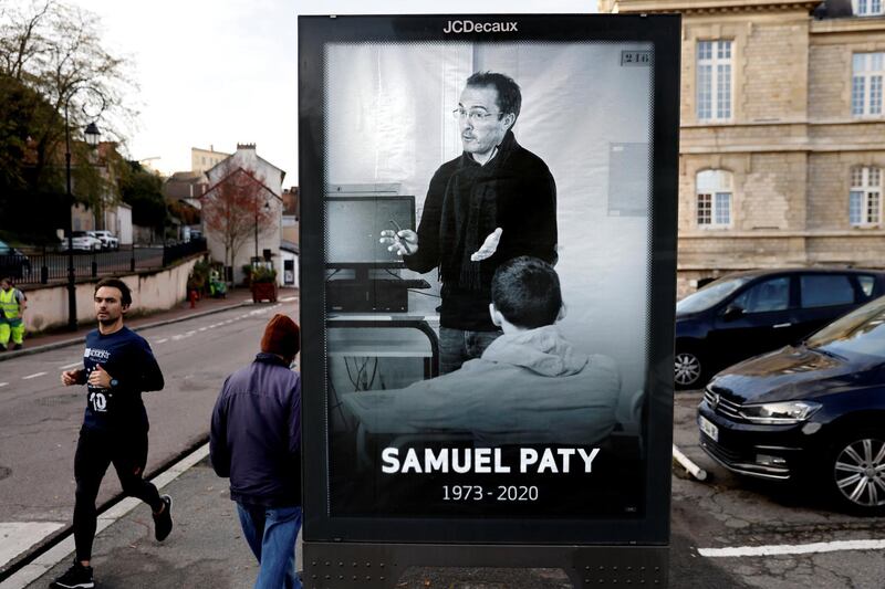Pedestrians pass by a poster depicting French teacher Samuel Paty placed in the city center of Conflans-Sainte-Honorine, 30kms northwest of Paris, on November 3, 2020, following the decapitation of the teacher on October 16. - France on November 2 honoured the teacher beheaded near his school in Conflans-Sainte-Honorine by a suspected Islamist radical as millions of students returned to class after autumn break and a spate of attacks that have put the country on edge. (Photo by Thomas COEX / AFP)