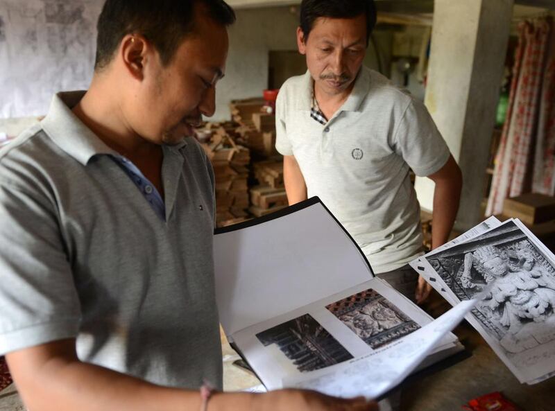 Nepalese woodcarver Indra Kaji Shilpakar, right, looks at images of carvings at his workshop in Bhaktapur on the outskirts of Kathmandu. Prakash Mathema / AFP