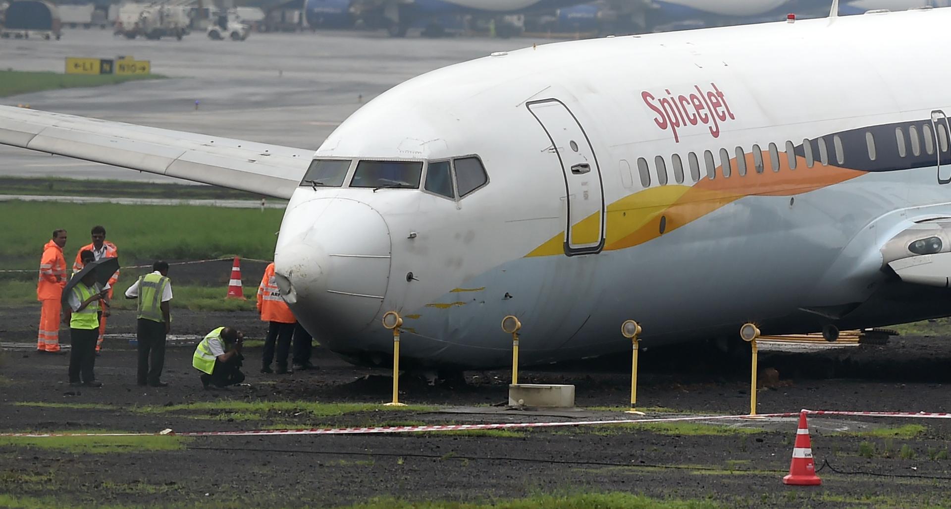 TOPSHOT - A SpiceJet aircraft is surrounded by airport staff as it stands stranded off the tarmac at Chhatrapati Shivaji Maharaj International Airport in Mumbai on July 2, 2019, after it overran the runway while landing during heavy rain, causing no injuries. / AFP / PUNIT PARANJPE
