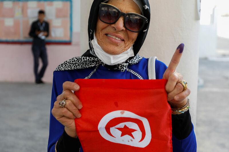 A woman shows her ink-stained finger as she holds the Tunisian flag at a polling station in Tunis. Reuters