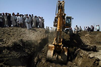 Iraqis watch as an excavator digs around an area where bodies were exhumed from a mass grave in May 2003, in Mahaweel. Getty