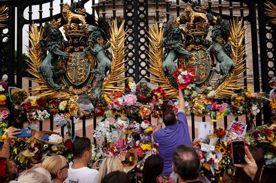 People place bouquets of flowers at the gates of Buckingham Palace. Getty