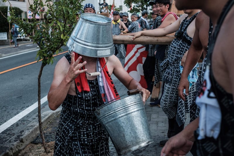 A man fools around with a water bucket on his head as participants rest before carrying fireworks to the Yoshida Shrine. AFP