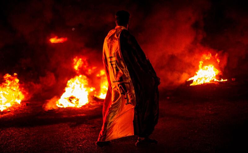 A protester draped in a national flag stands by a fire in Basra. AFP