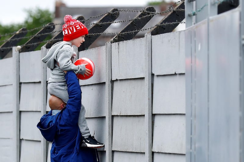 A Liverpool fan is held up as he looks over a fence to watch training at Melwood. Reuters