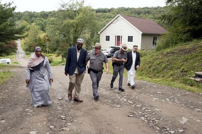 In this Sept. 7, 2017 photo, Tahirah Clark, left, and Faruq Baqi walk with New York State Police Capt. Scott Heggelke, center, in the Muslim enclave of Islamberg in Tompkins, N.Y. With them are Maj. James Barnes, second from right, and Muhammad Matthew Gardner, right, a spokesman for The Muslims of America. The troopers were making a goodwill visit to the village. "These folks that live here are American citizens. They're lived here for over 30 years. They built this community. They have ties within, outside of this community," Barnes said. "And there's not a problem here." (AP Photo/Mark Lennihan)