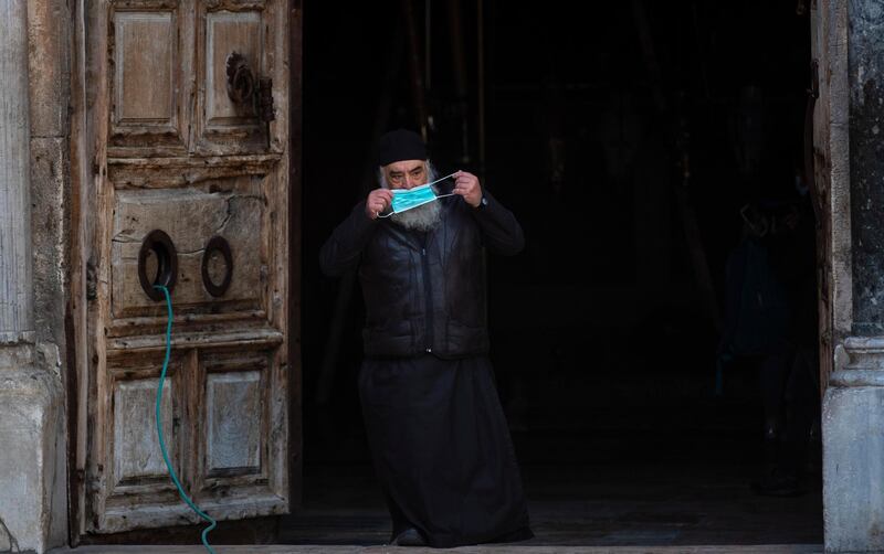 An Orthodox Christian clergy member puts on his face mask while walking out of the Church of Holy Sepulchre in Jerusalem’s Old City.