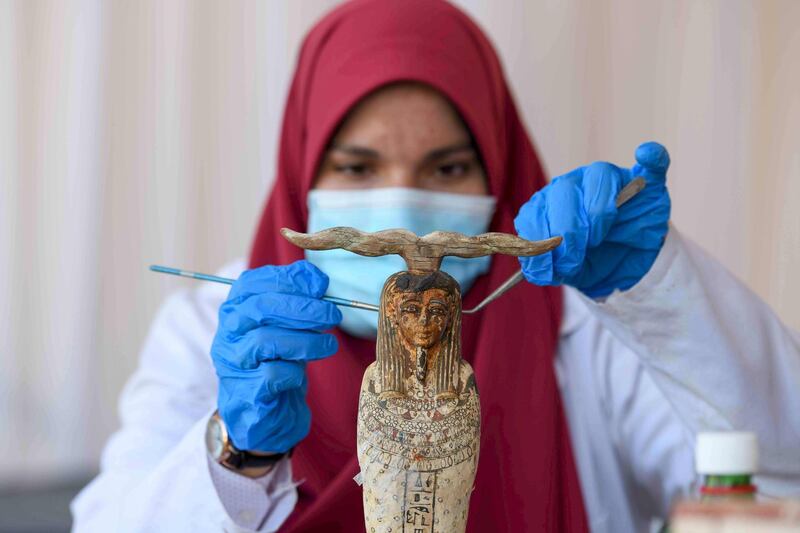 An archaeologist cleans a statue during the unveiling of an ancient treasure trove of more than a 100 intact sarcophagi. AFP